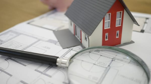 Model house on a blueprint with a magnifying glass